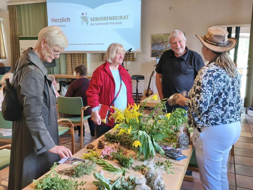 Vier ältere Menschen stehen an einem Tisch mit Blumen und Pflanzen in einem Veranstaltungsraum.