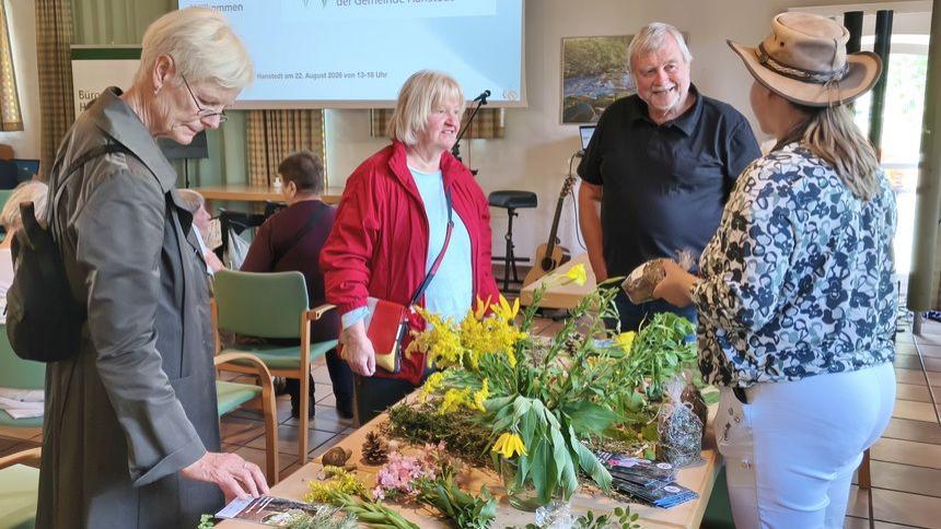 Vier ältere Menschen stehen an einem Tisch mit Blumen und Pflanzen in einem Veranstaltungsraum.